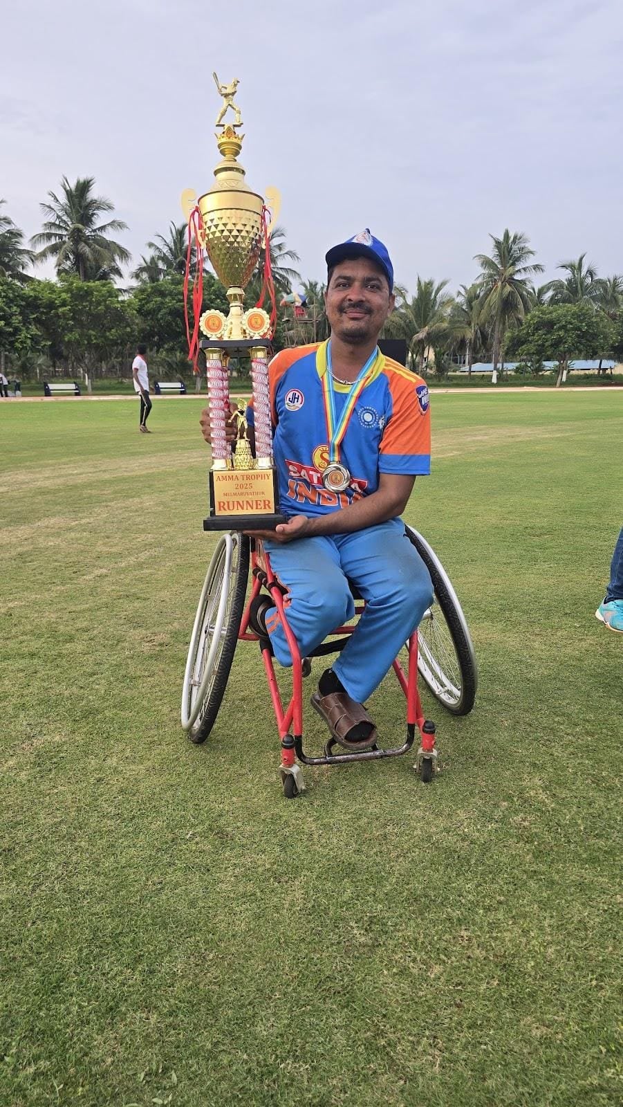 Hareesh Kumar in a sports wheelchair holding a large trophy on the ground